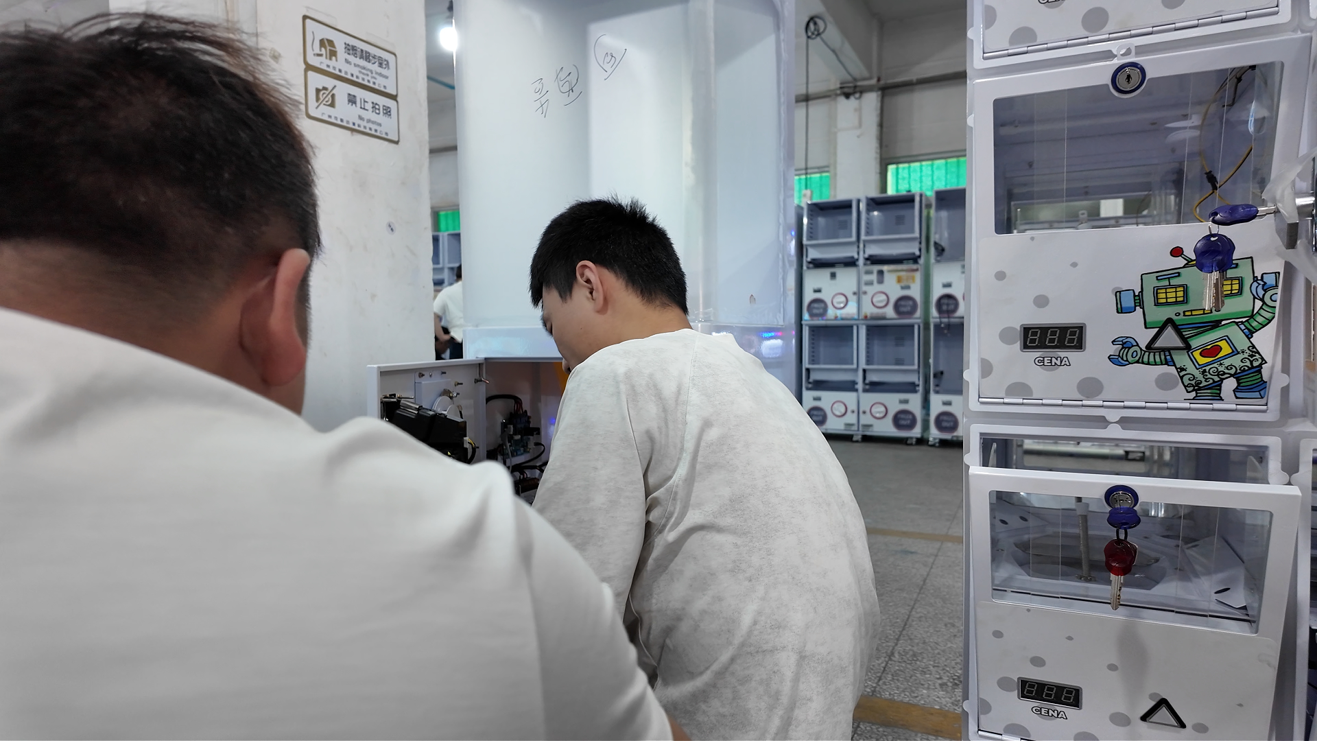 Two factory technicians assemble and test customized cartoon pattern capsule vending machines in production workshop