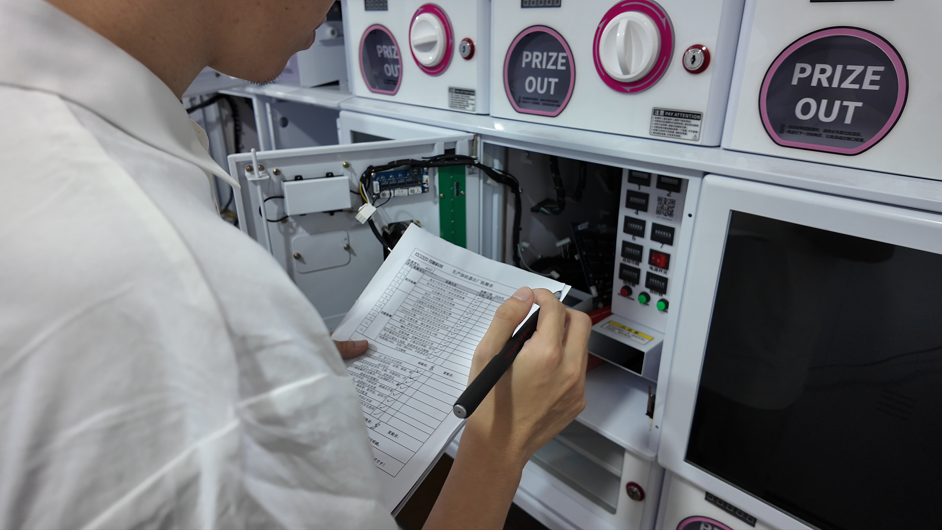 QC inspector fills out test checklist to inspect the internal circuit of prize vending machines in factory workshop